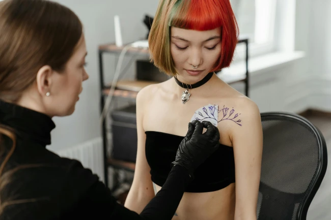 Mujer tatuando a otra en el pecho